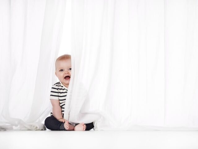 Baby kigger frem bag et hvidt gardin